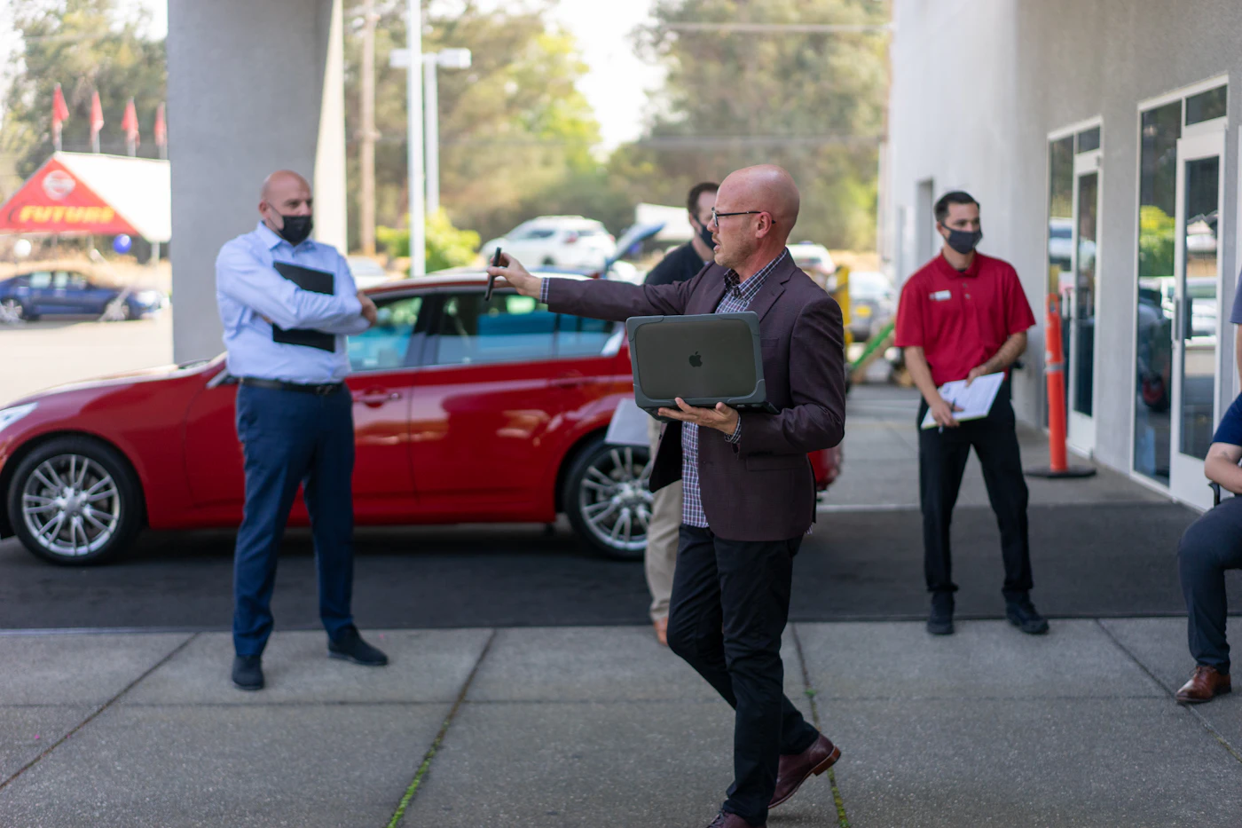A salesperson with a tablet talking with customers next to a car